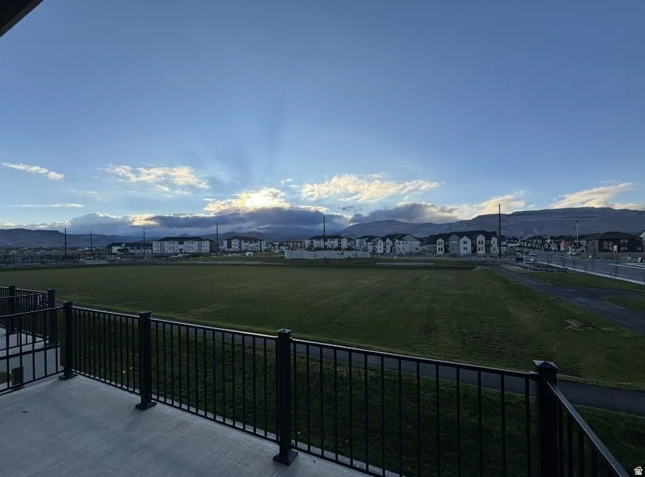 Balcony with black metal railing overlooking a large green field and distant mountains