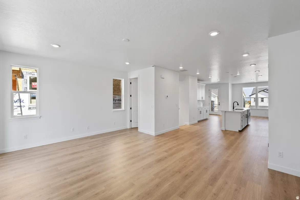 Open-concept living space featuring light wood-finish flooring, recessed lighting, white walls, and white baseboards
