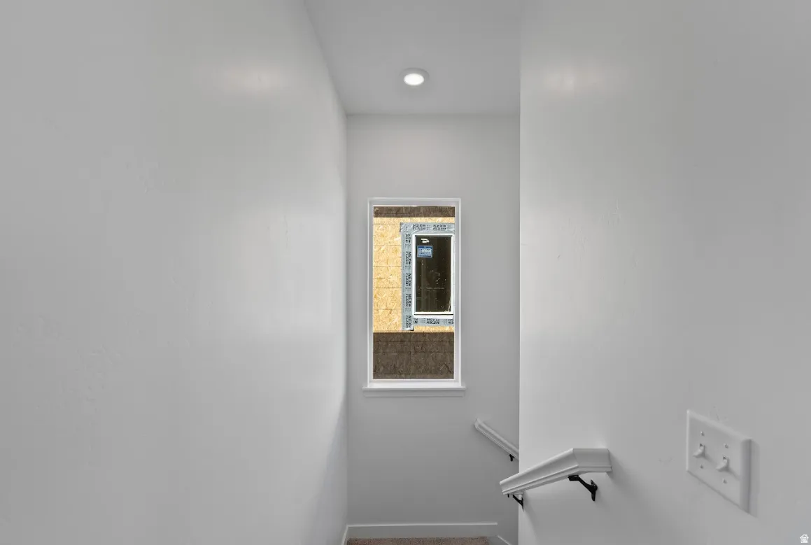 Recessed ceiling lighting illuminating a bright white painted stairwell featuring a single window and white handrail