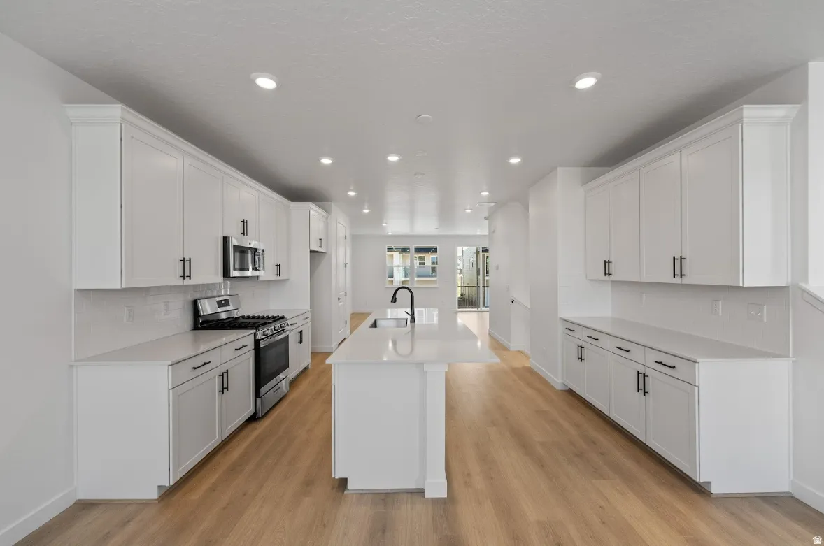 Modern kitchen featuring extensive white cabinetry with matte black hardware, stone countertops, and wood-finish flooring