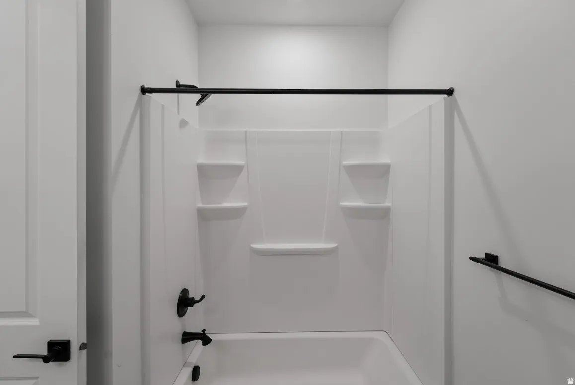 Bathtub and shower combination with white surround, integrated shelving, and matte black fixtures