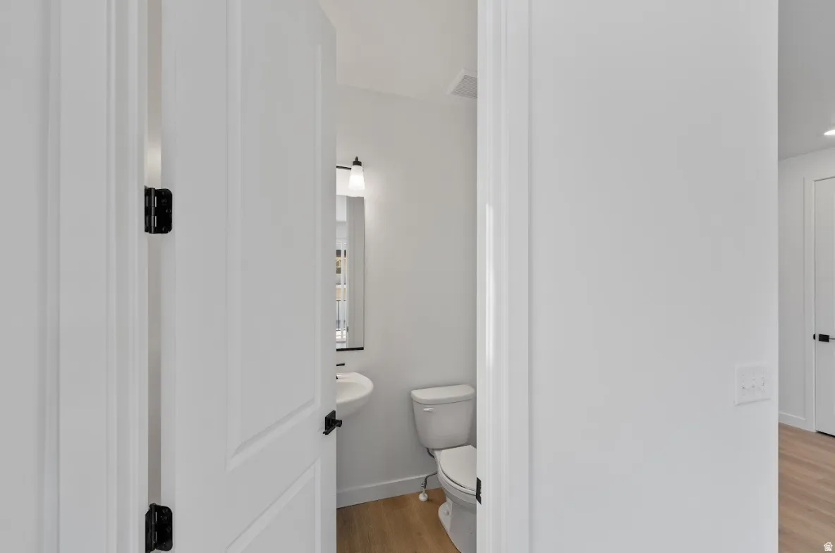 Bright powder room featuring a wall-mounted sink, toilet, and wood-finish flooring