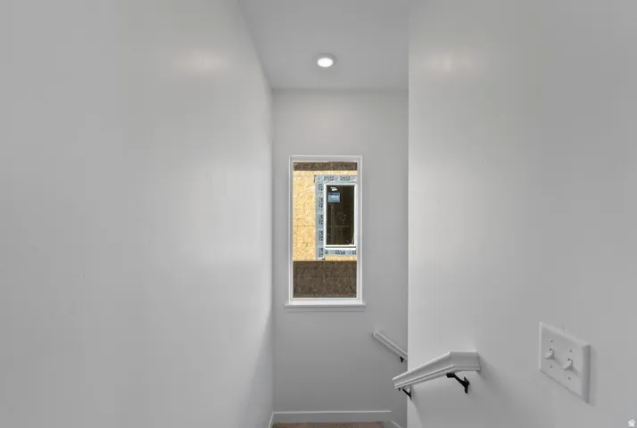 Recessed ceiling lighting illuminating a bright white painted stairwell featuring a single window and white handrail
