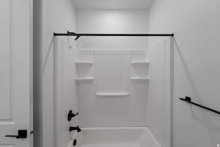 Bathtub and shower combination with white surround, integrated shelving, and matte black fixtures