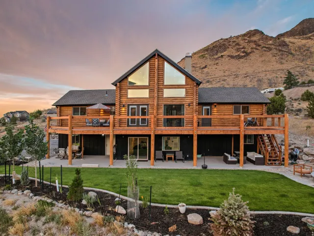 Log cabin exterior with a multi-level deck, expansive windows, and a manicured lawn