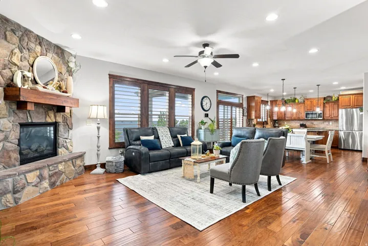 Stone-clad fireplace with a wood mantle, hardwood flooring, recessed lighting, and kitchen with pendant lights