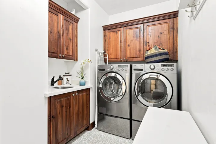 Laundry room on main floor featuring wood-finish cabinetry, a white countertop, an undermount sink, and patterned floor tile