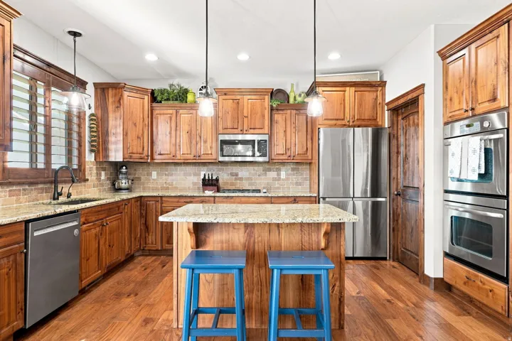 Wood-finish flooring, wood cabinetry, stone countertops, stainless steel appliances, and a tiled backsplash