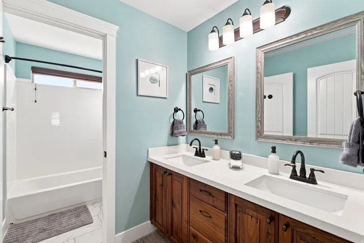 Upstairs full bathroom. Dual rectangular undermount sinks, white countertop, wood-finish cabinetry, framed mirrors, and a four-light fixture
