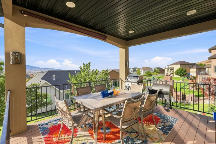 Expansive covered deck featuring composite decking, wrought iron railings, integrated ceiling lighting, and a stucco-clad column