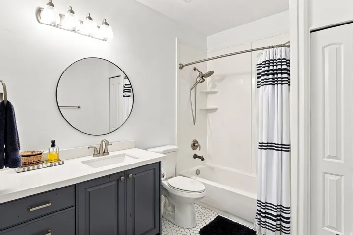 Basement full bathroom. White bathroom with a dark blue vanity, white countertop, and circular mirror