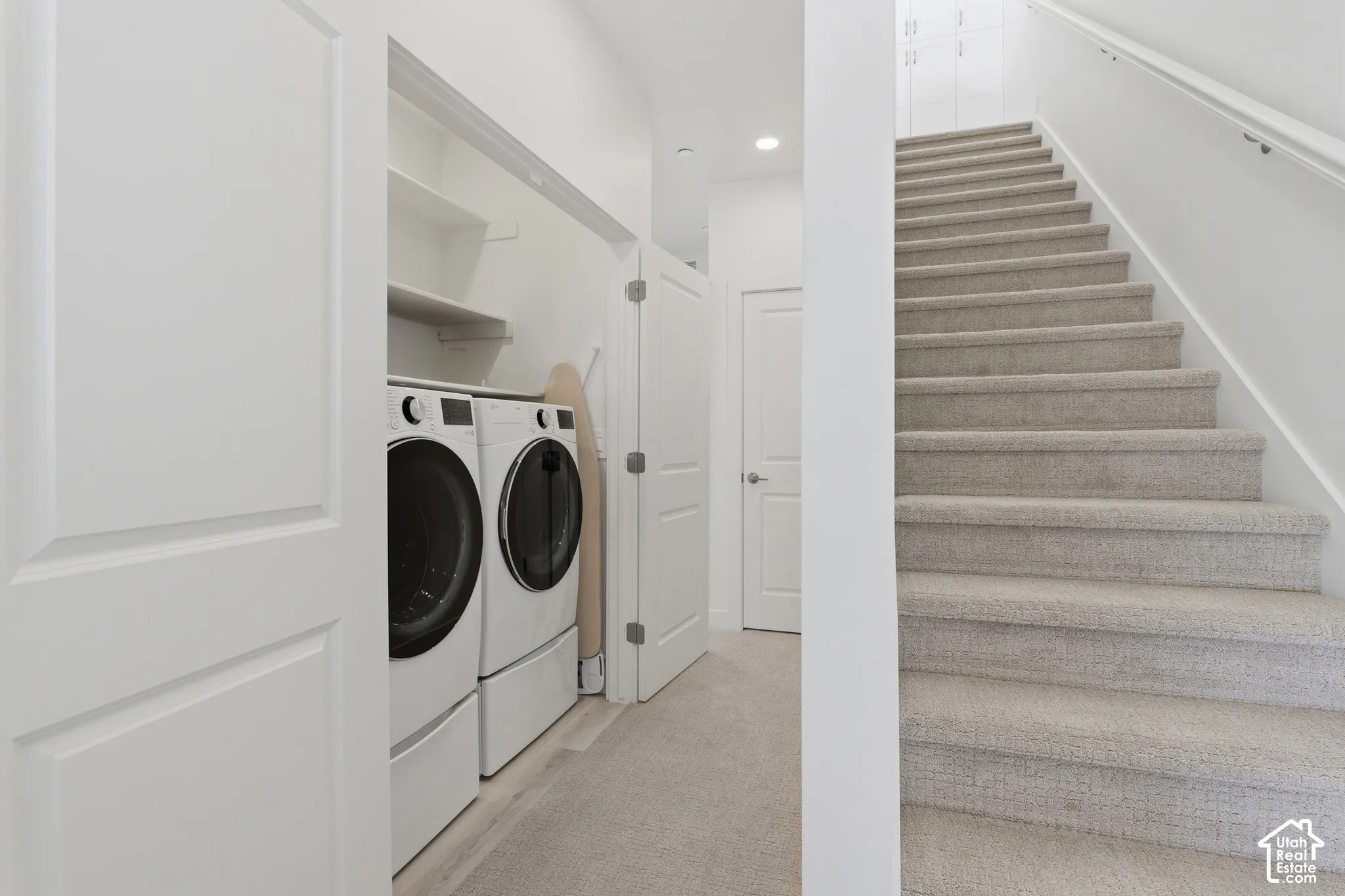Full-size laundry appliances with built-in shelving, complemented by a carpeted staircase with a white handrail