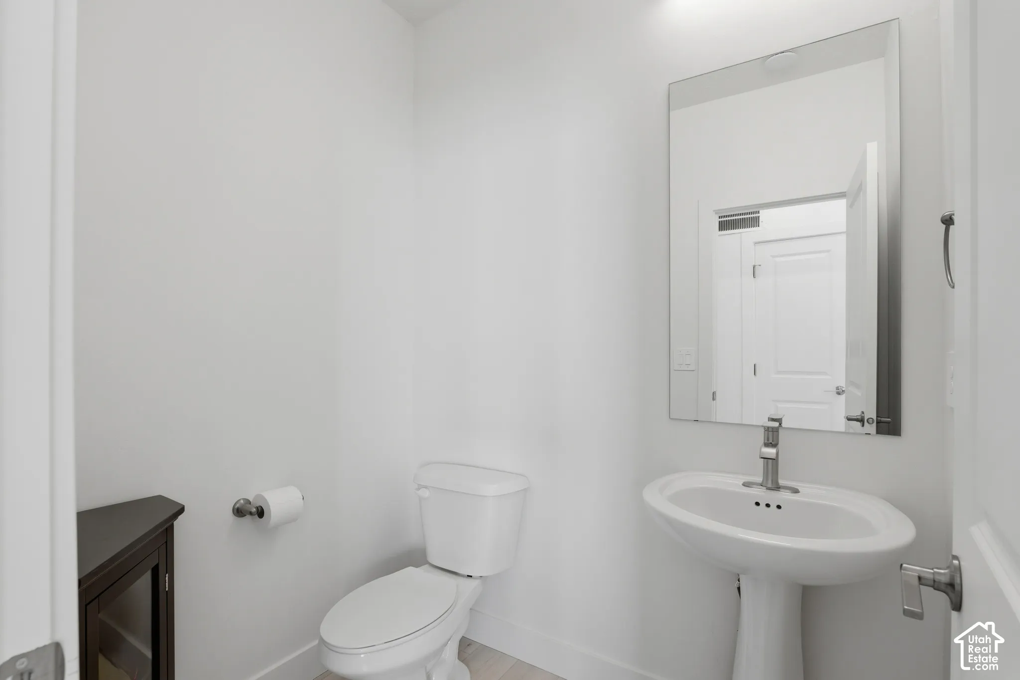 Pedestal sink with a polished chrome faucet, rectangular wall-mounted mirror, and a dark wood-finish corner cabinet