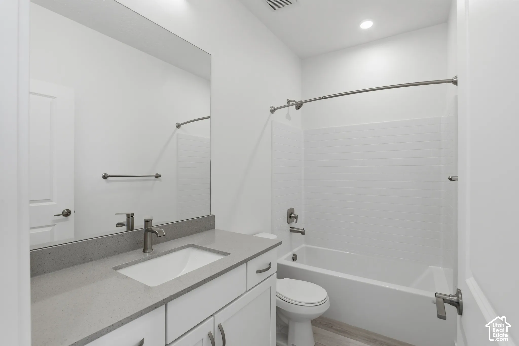 Modern bathroom featuring a single vanity with a gray countertop, an integrated rectangular sink, a brushed nickel faucet, and a white bathtub with a subway tile surround