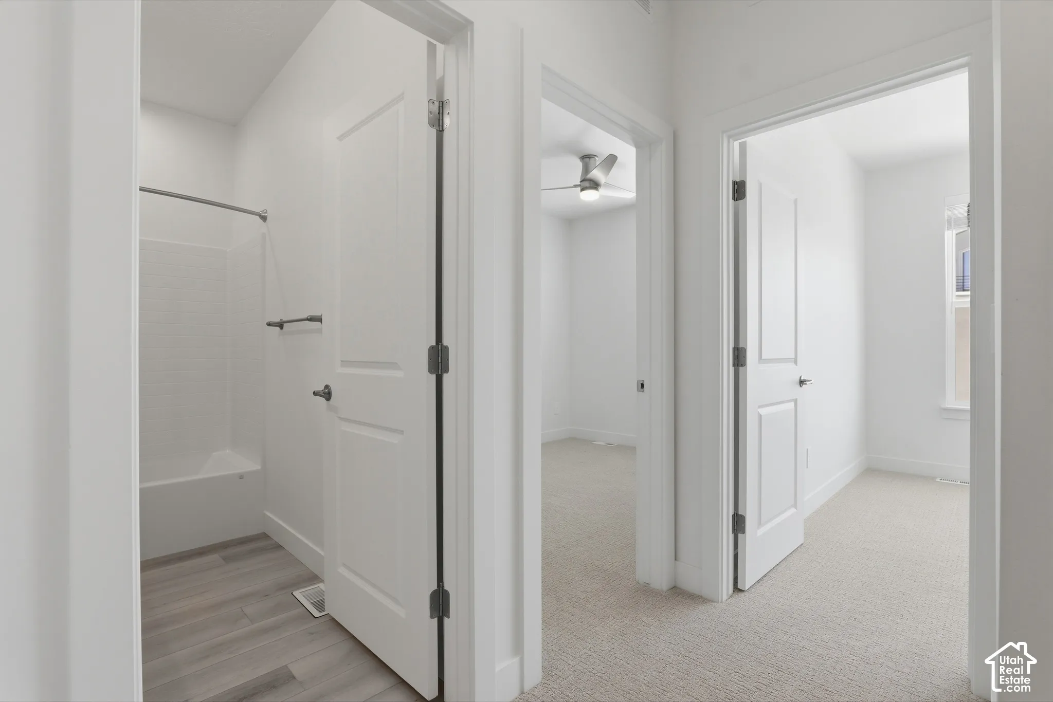 White interior doors, neutral carpeting, wood-finish flooring, white walls, and a ceiling fan