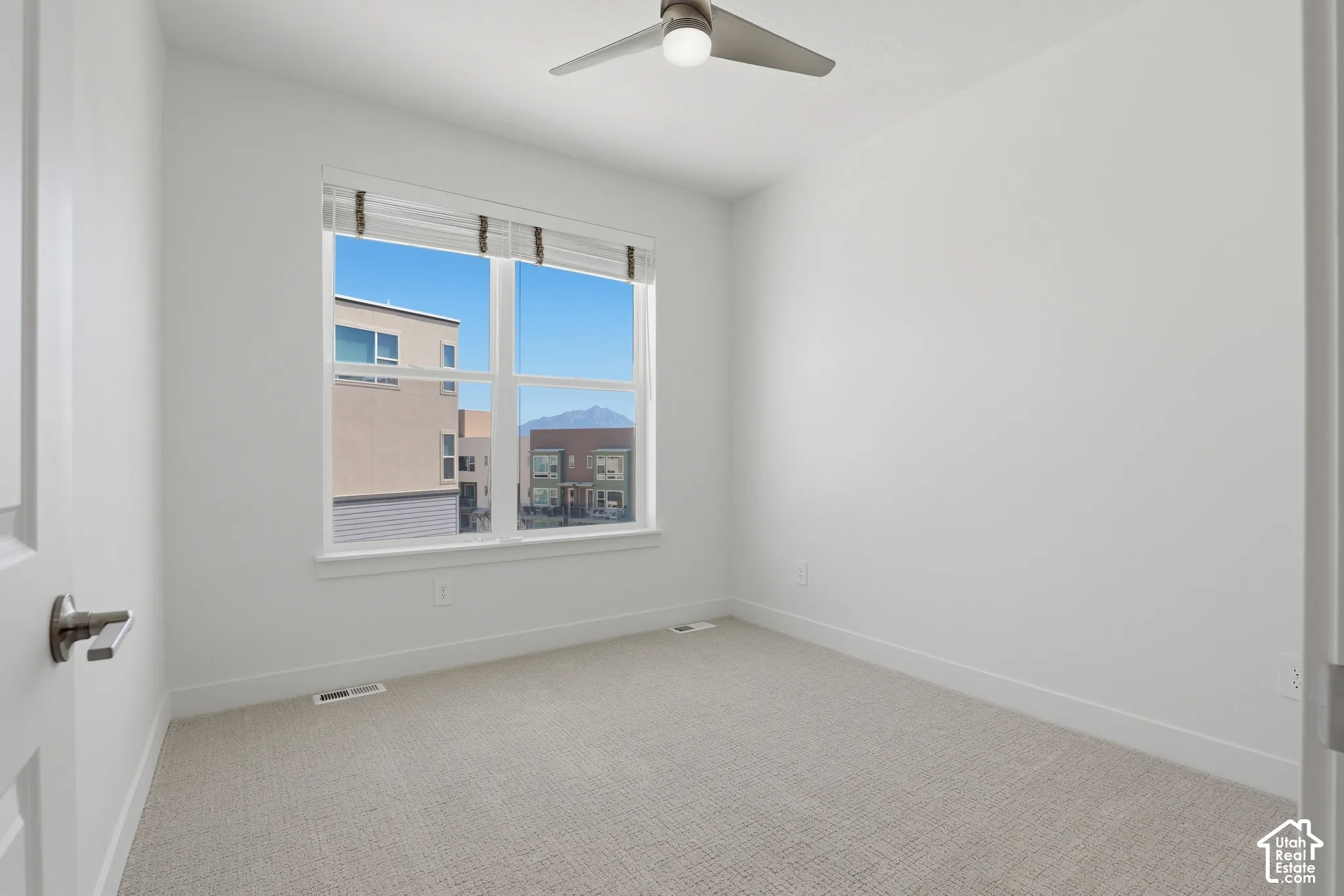 White walls with carpeted flooring, featuring a window with blinds, and a ceiling fan with integrated lighting