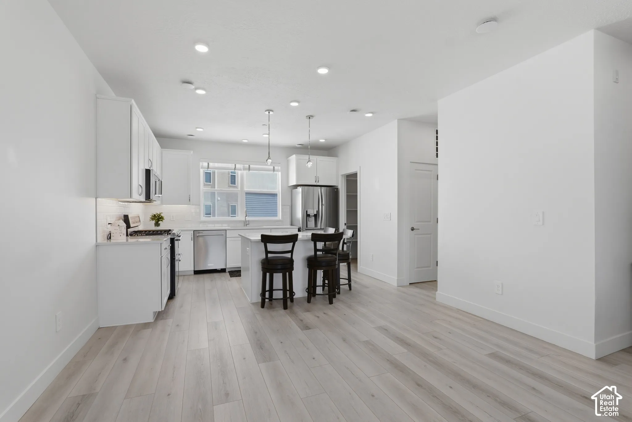 Kitchen featuring white cabinetry, stainless steel appliances, a center island with pendant lighting, and wood-finish flooring