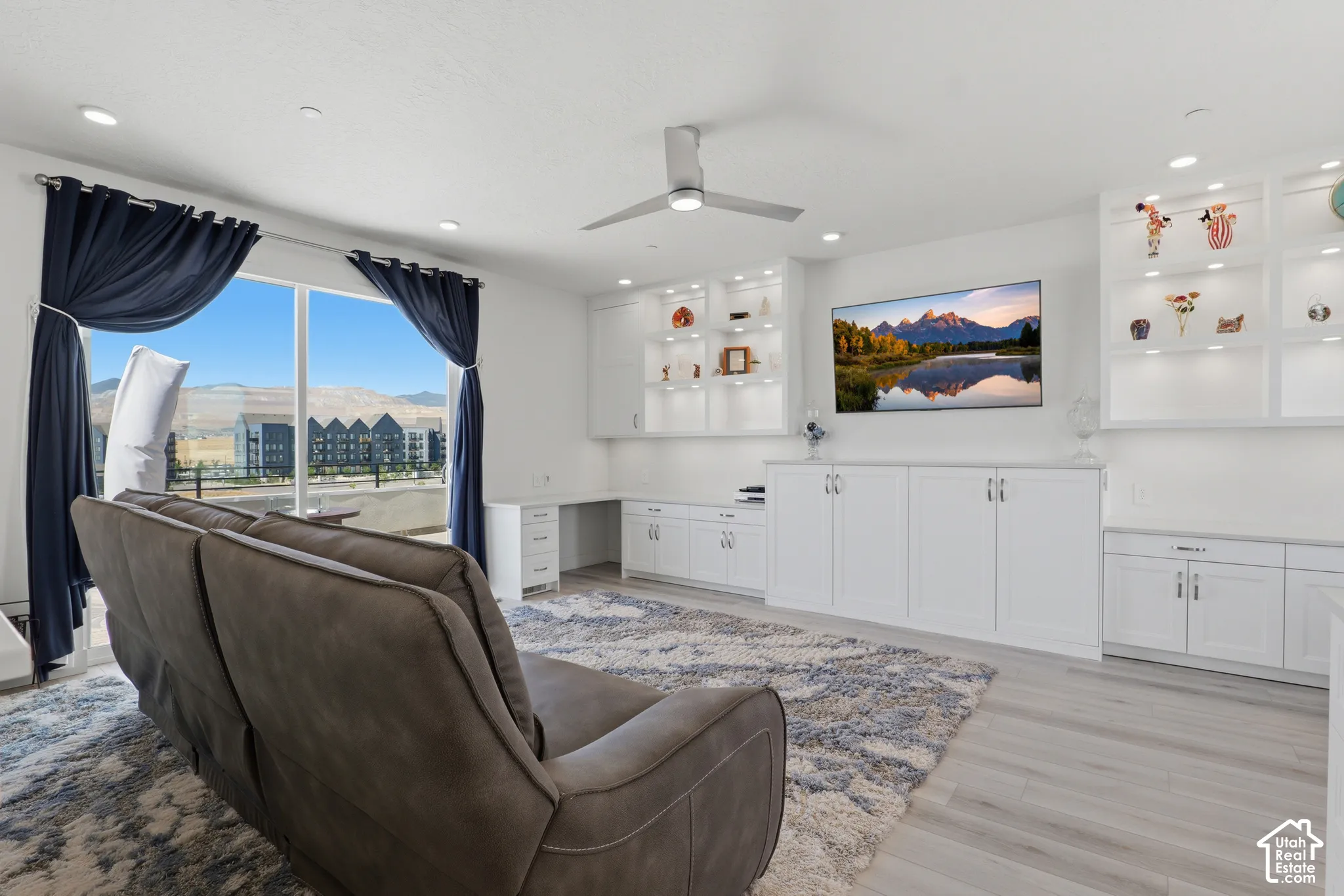 Built-in shelving with integrated lighting, extensive white cabinetry with solid surface countertops, recessed ceiling lights, a ceiling fan, and light wood-finish flooring