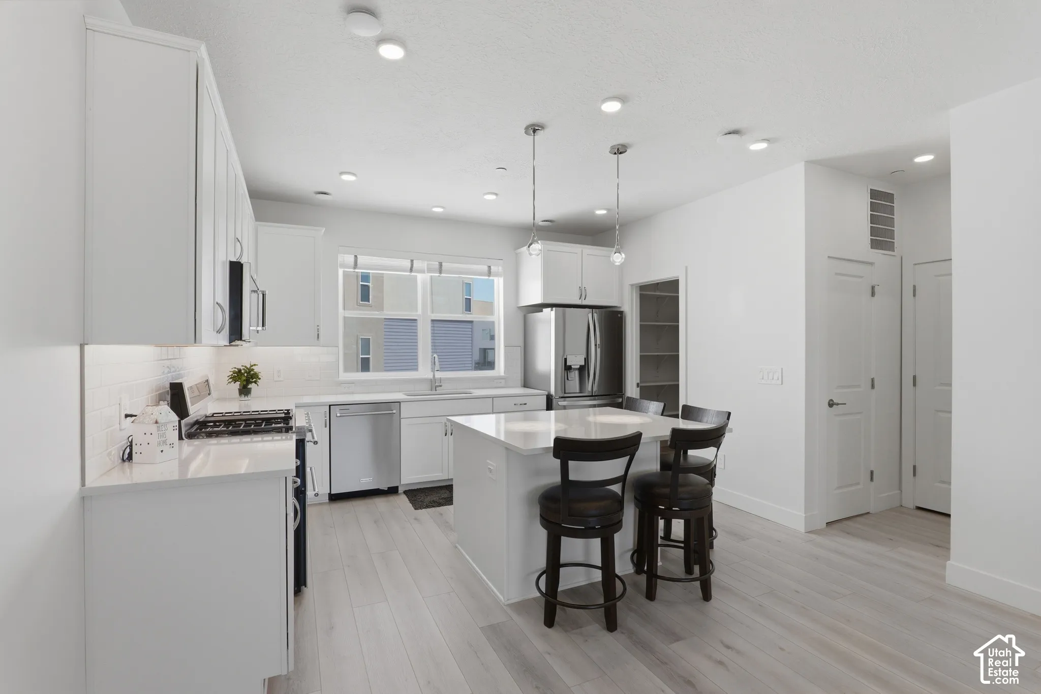 Bright kitchen featuring white cabinetry, stainless steel appliances, light wood-finish flooring, a central island with seating, and recessed lighting