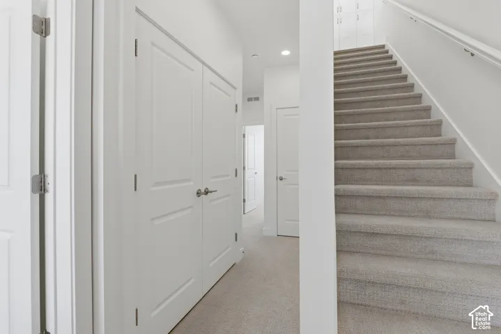 Carpeted staircase with white handrail, recessed lighting, and white paneled doors