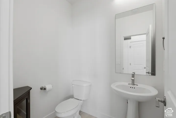 Pedestal sink with a polished chrome faucet, rectangular wall-mounted mirror, and a dark wood-finish corner cabinet