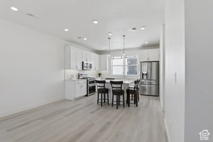 Open-concept kitchen with white cabinetry, stainless steel appliances, and a central island with pendant lighting