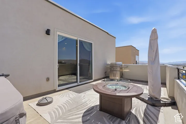 Expansive rooftop patio with a stainless steel grill, a built-in fire pit, and a sliding glass door entry