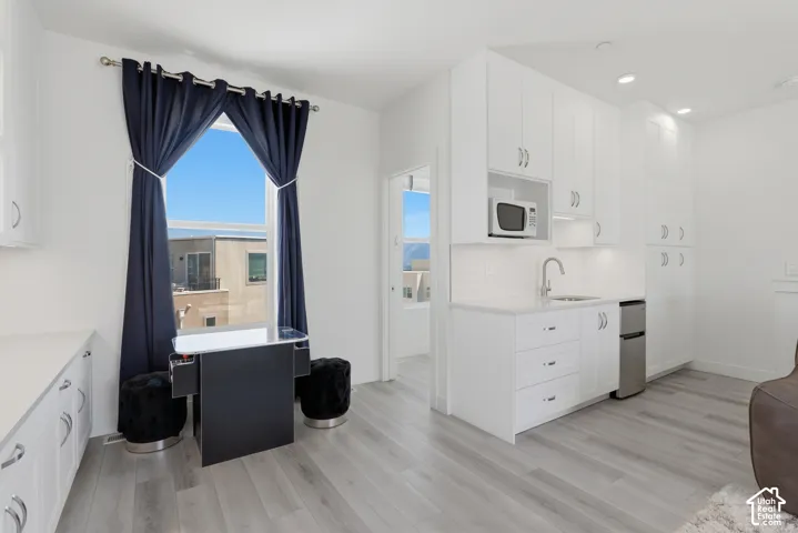 White cabinetry with brushed nickel hardware, stainless steel sink, built-in microwave, and wood-finish flooring