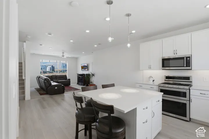 Open-concept design featuring a modern kitchen island with seating, stainless steel appliances, white cabinetry, and recessed lighting