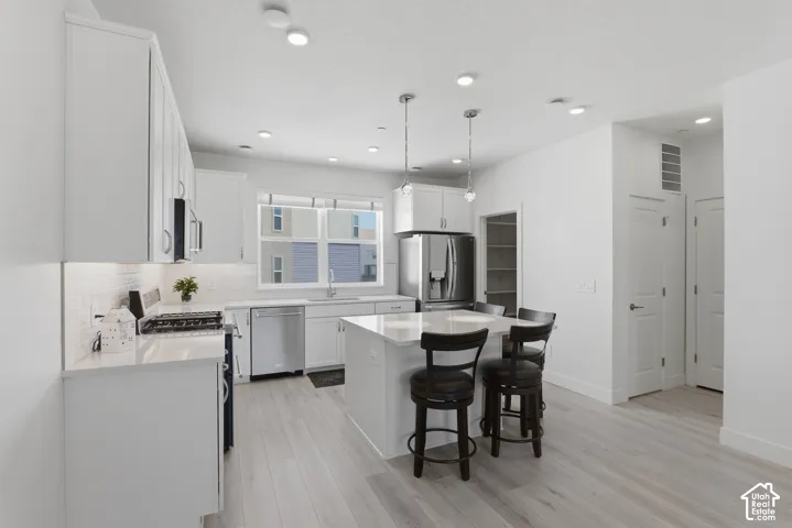 Bright kitchen featuring white cabinetry, stainless steel appliances, light wood-finish flooring, a central island with seating, and recessed lighting