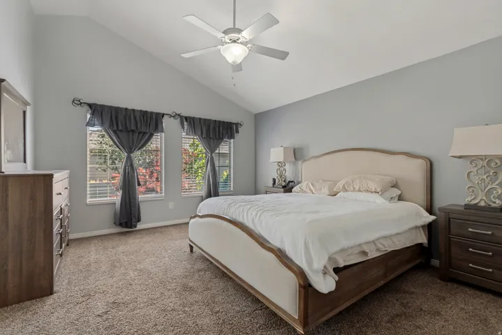 Vaulted ceiling with a ceiling fan, two windows, and carpet flooring