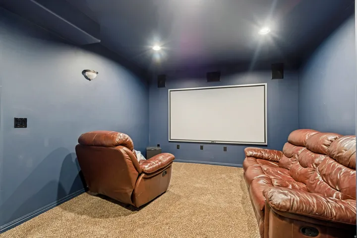 Dedicated theater room featuring a large projector screen, built-in wall speakers, recessed ceiling lighting, and wall sconce lighting
