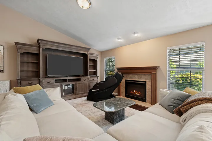 Living area featuring a vaulted ceiling, recessed lighting, a built-in entertainment center, a tiled fireplace with a wood mantel, and multiple windows with blinds