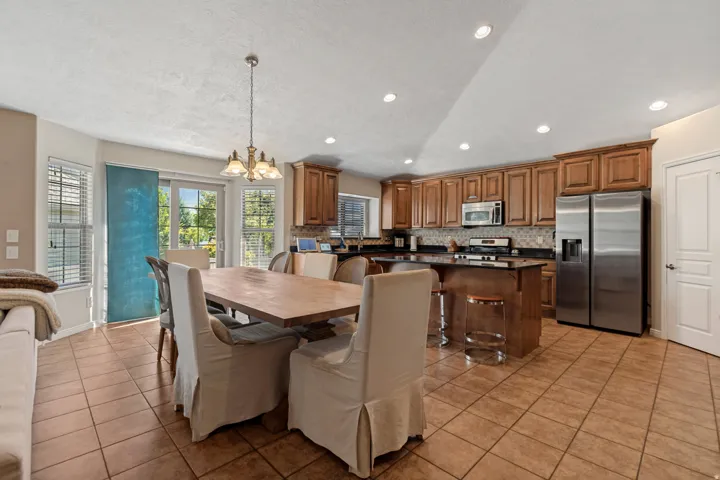 Kitchen and dining area featuring tile flooring, wood cabinetry, stainless steel appliances, and a central island with bar seating