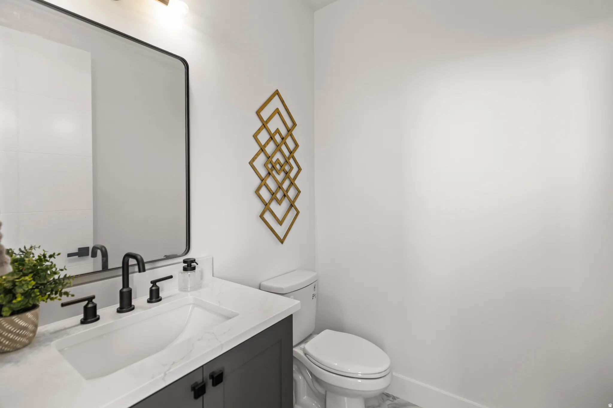 Modern bathroom featuring a black vanity with a white countertop and integrated sink, a black framed mirror, and a wall-mounted light fixture