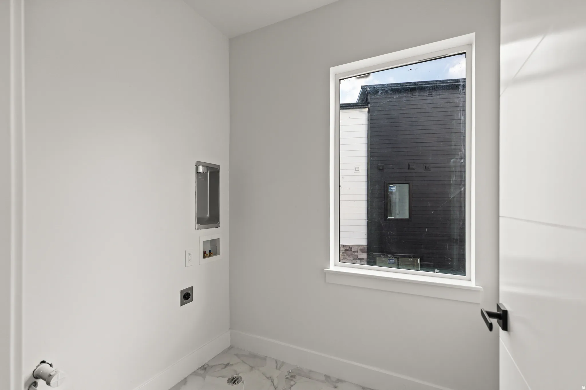 Laundry area with a single casement window, light-toned walls, and marble-finish flooring