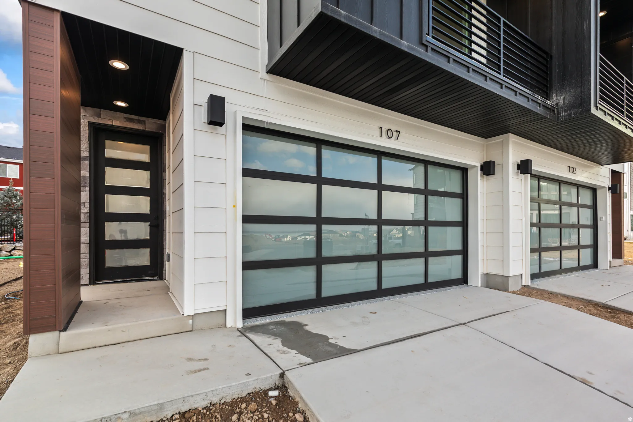Modern exterior featuring horizontal siding, glass-paneled garage doors, a dark wood-finish column, and recessed entry lighting