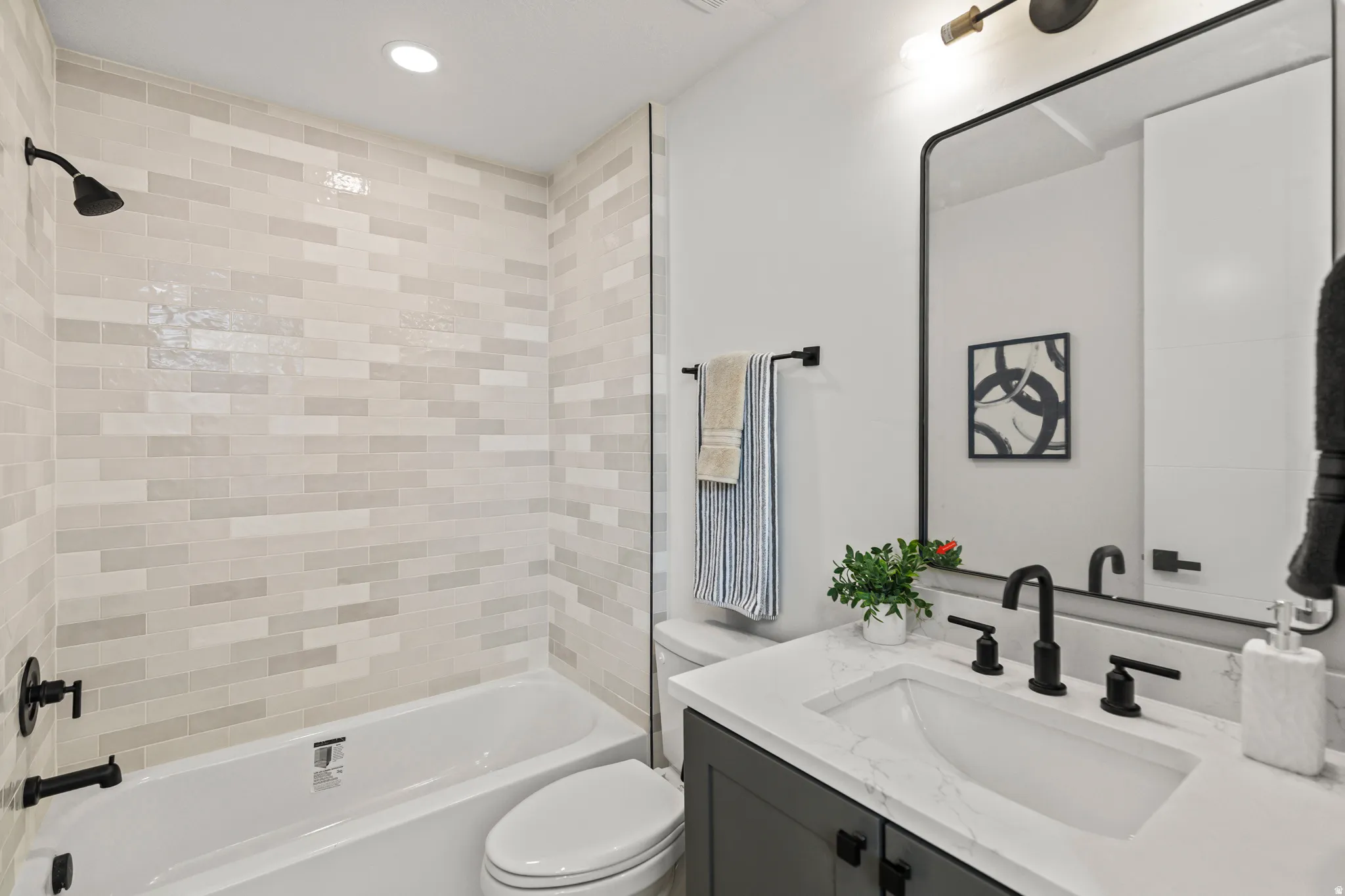 Bathtub with subway tile surround, matte black fixtures, dark wood-finish vanity, and a rectangular framed mirror