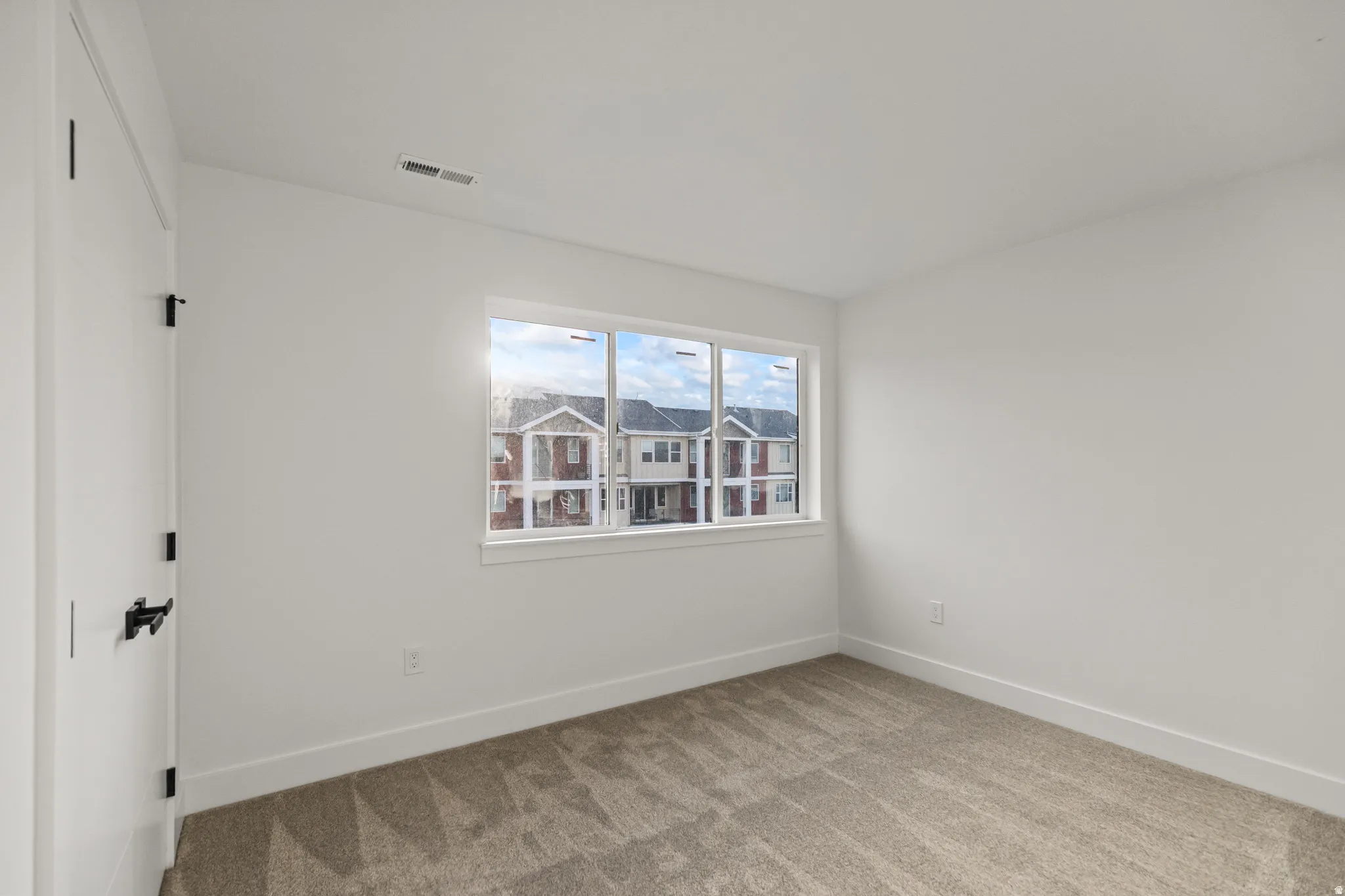 Neutral tone wall paint, contemporary black door hardware, white trim, and light-colored carpeting
