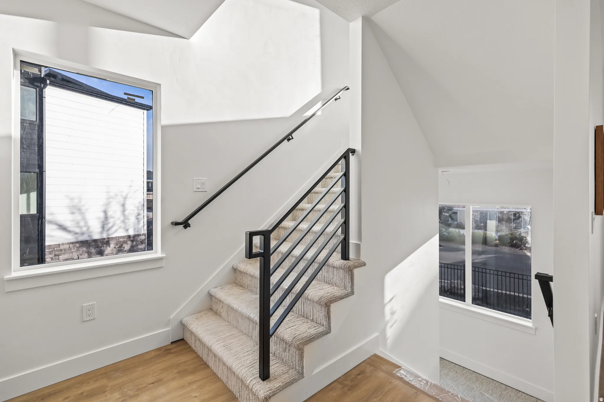 Modern staircase with black metal railing, carpeted treads, and wood-finish flooring