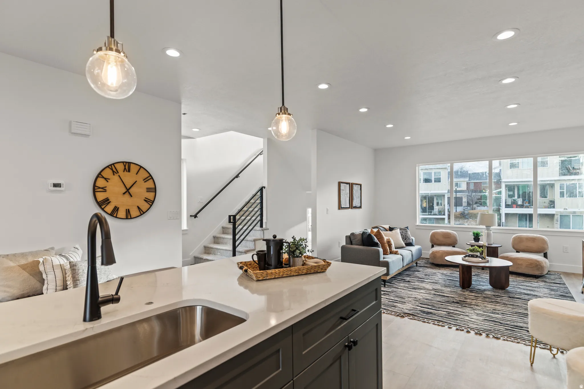 Open-concept living space featuring a kitchen island with a stainless steel sink, recessed lighting, wood-finish flooring, and a staircase with a black metal railing