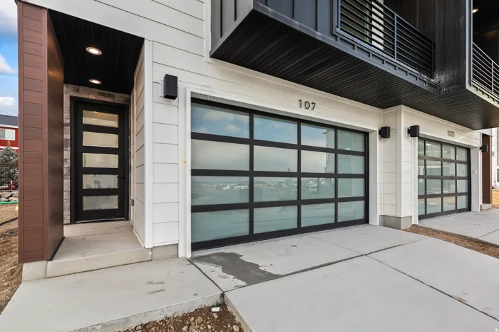 Modern exterior featuring horizontal siding, glass-paneled garage doors, a dark wood-finish column, and recessed entry lighting
