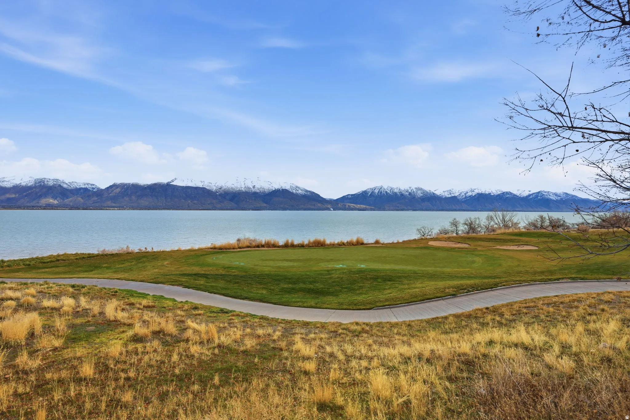Expansive golf course green with sand traps, a paved cart path, and a lake