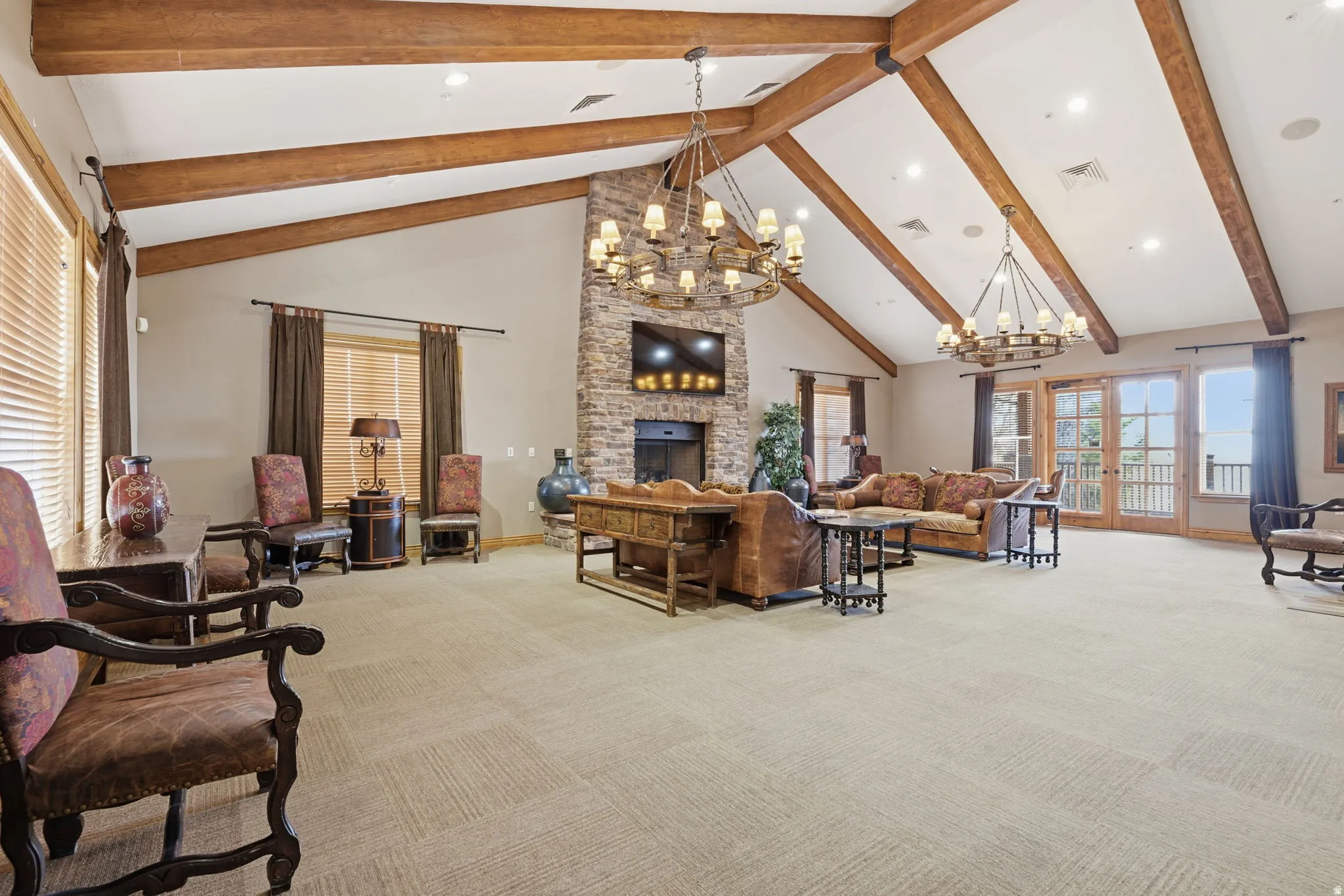 Vaulted ceilings with exposed wood beams, stone-clad fireplace, French doors, carpet flooring, and multiple windows