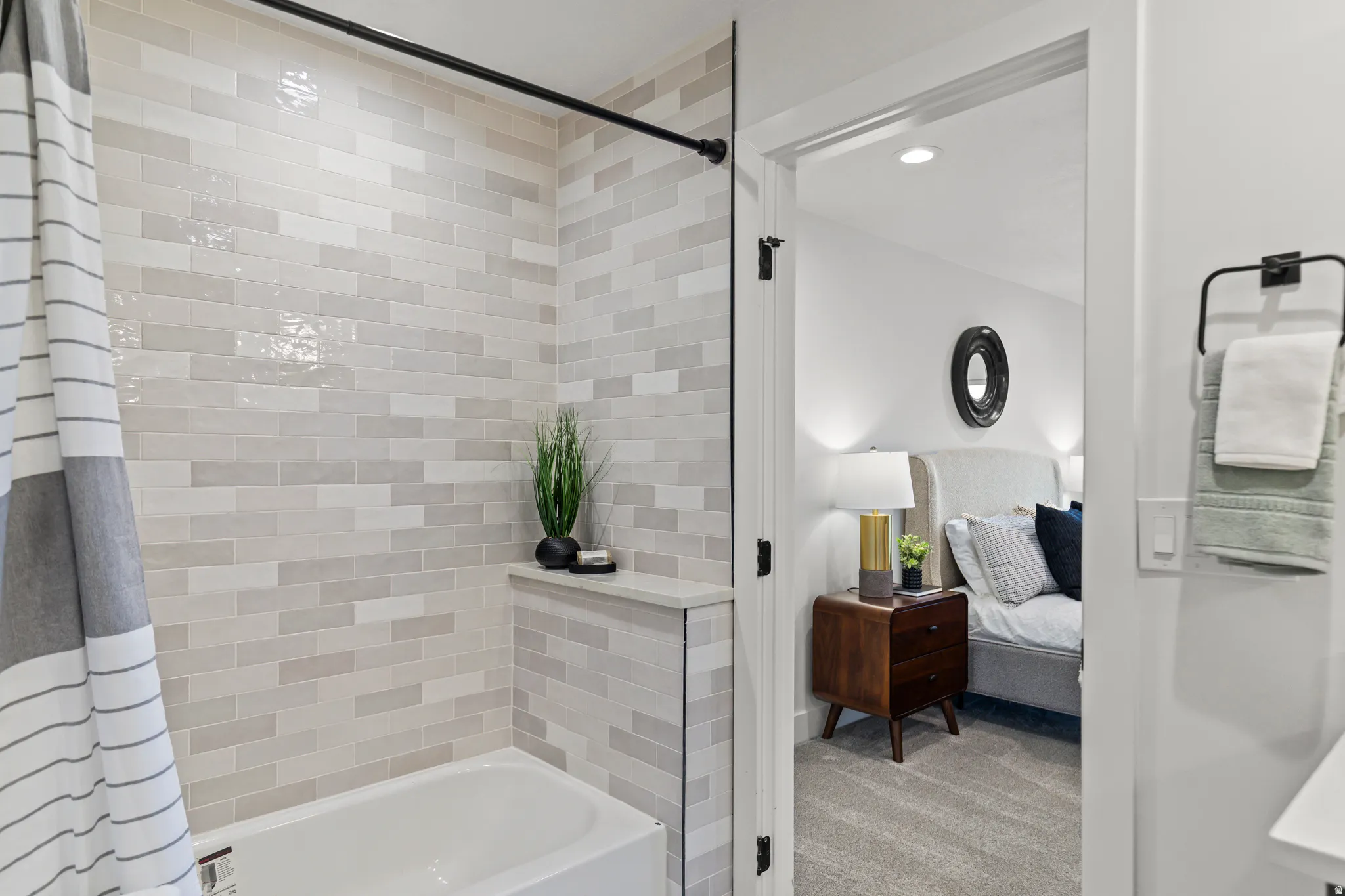 Built-in bathtub with subway tile surround, integrated shelf, and black shower rod