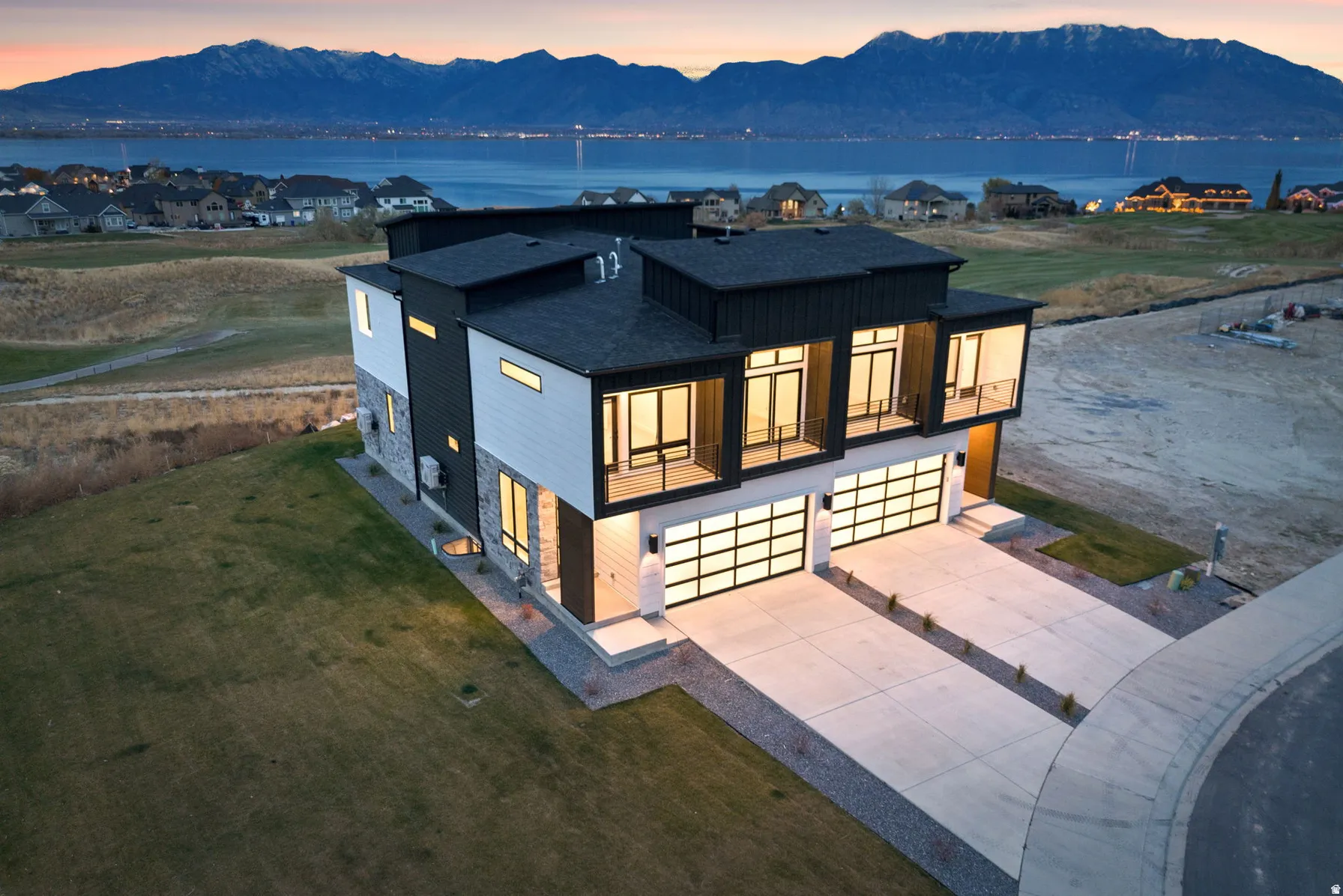 Modern architectural design featuring expansive windows, multiple balconies, a three-car garage with translucent doors, and a combination of vertical siding and stone accents