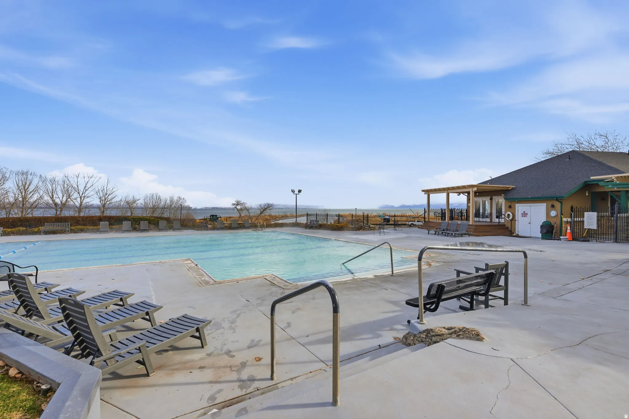 Outdoor swimming pool with concrete decking, a building featuring an exterior covered patio, and a distant body of water