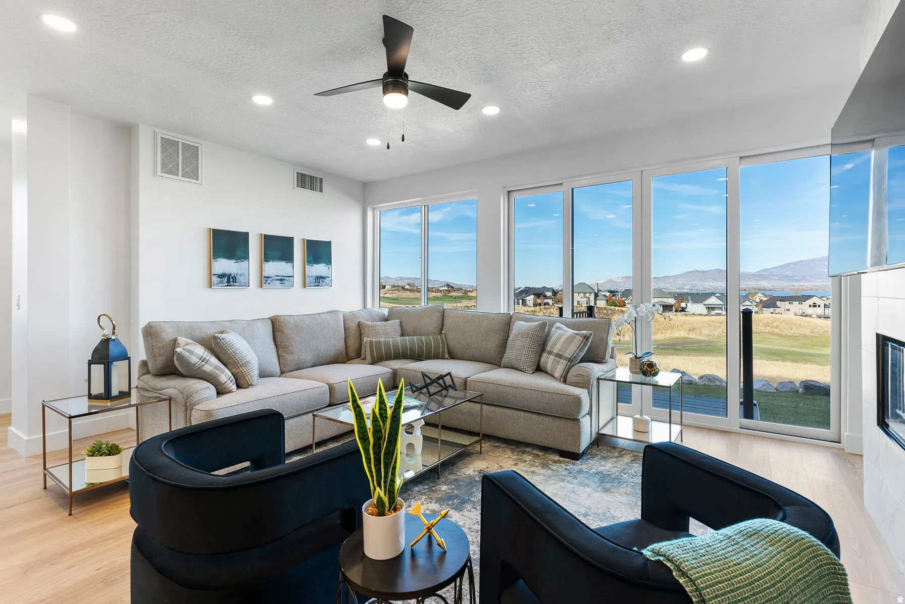 Expansive windows, light wood-finish flooring, recessed lighting, and a contemporary ceiling fan