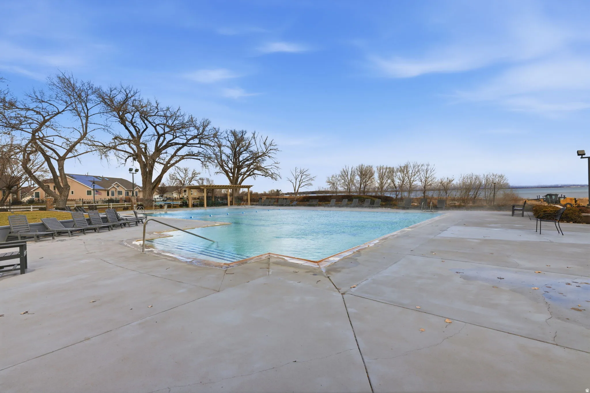 Expansive outdoor pool with concrete decking, surrounding green space, and mature trees