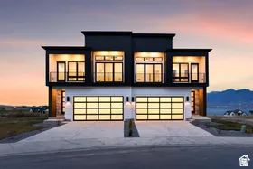 Contemporary architecture with a flat roofline, black and white exterior siding, expansive windows, two prominent balconies with railings, and modern garage doors